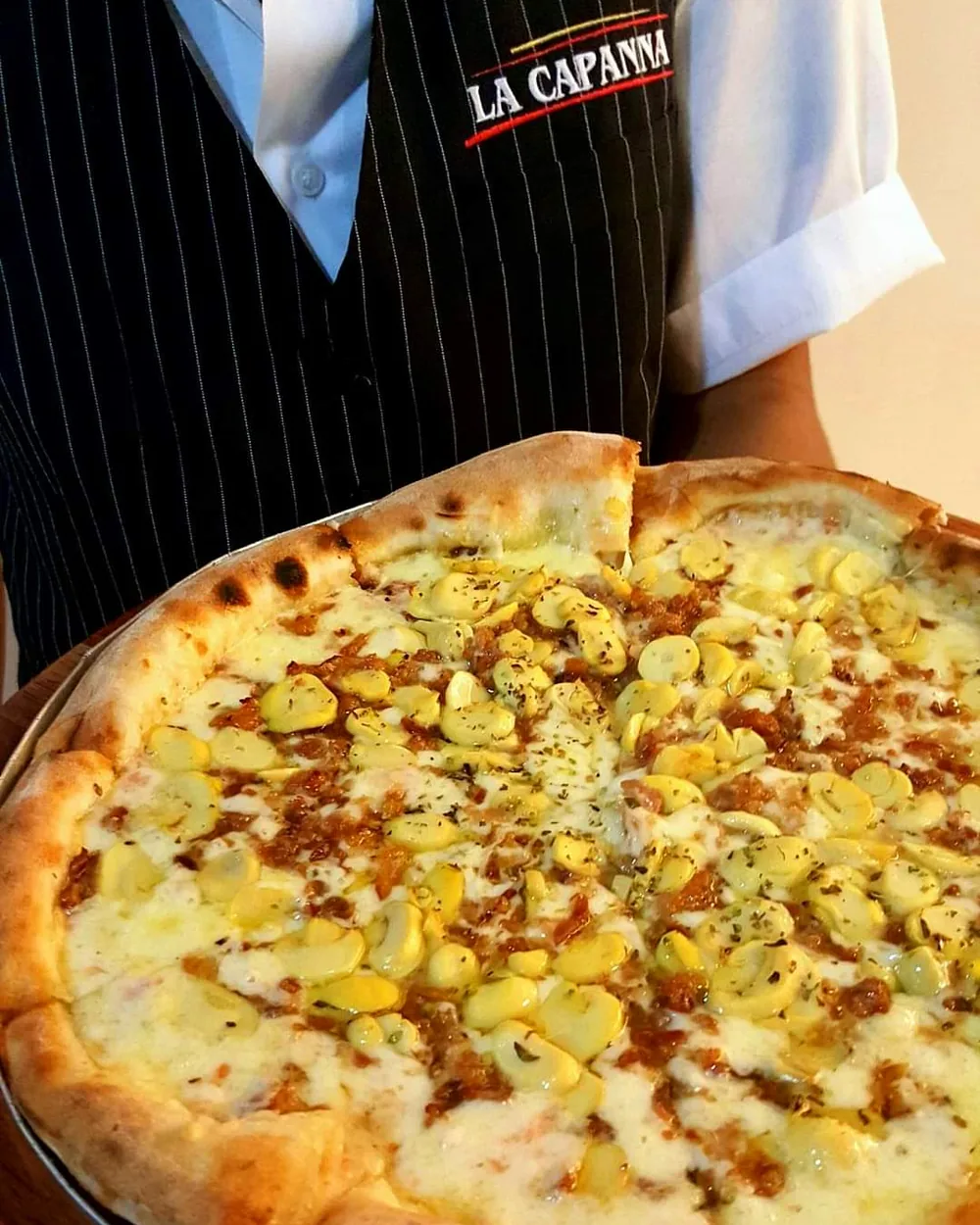 Atendente da La Capanna com uma pizza recém-saída do forno